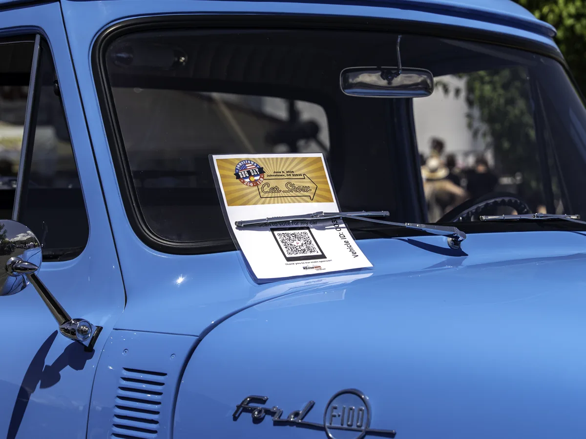 QR voting placard resting on the windshield of a classic Ford F-100 at a live car show